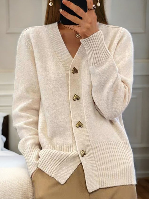 Femme portant un cardigan beige élégant avec boutons en forme de cœur, manches longues, col en V, dans une pièce lumineuse. Mode automne chic.