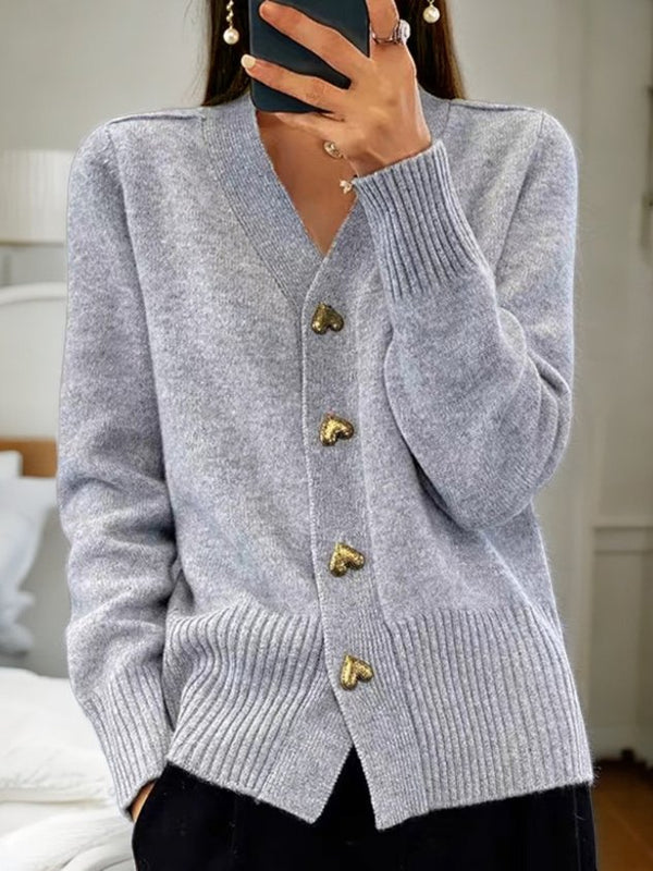 Femme portant un cardigan gris en laine avec boutons en forme de cœur dorés, style décontracté chic, mode automne-hiver, intérieur moderne.