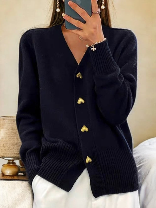 Femme portant un cardigan noir avec boutons dorés en forme de cœur, tenant un smartphone. Mode automne, style élégant et décontracté.