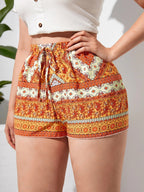 Short en tissu imprimé bohème orange et blanc, taille haute avec ceinture à nouer, porté par une femme. Mode estivale, style décontracté et tendance.