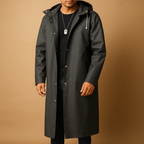 Homme portant un imperméable noir élégant avec capuche, fond beige. Mode masculine, manteau imperméable, style urbain, vêtement d'extérieur moderne.