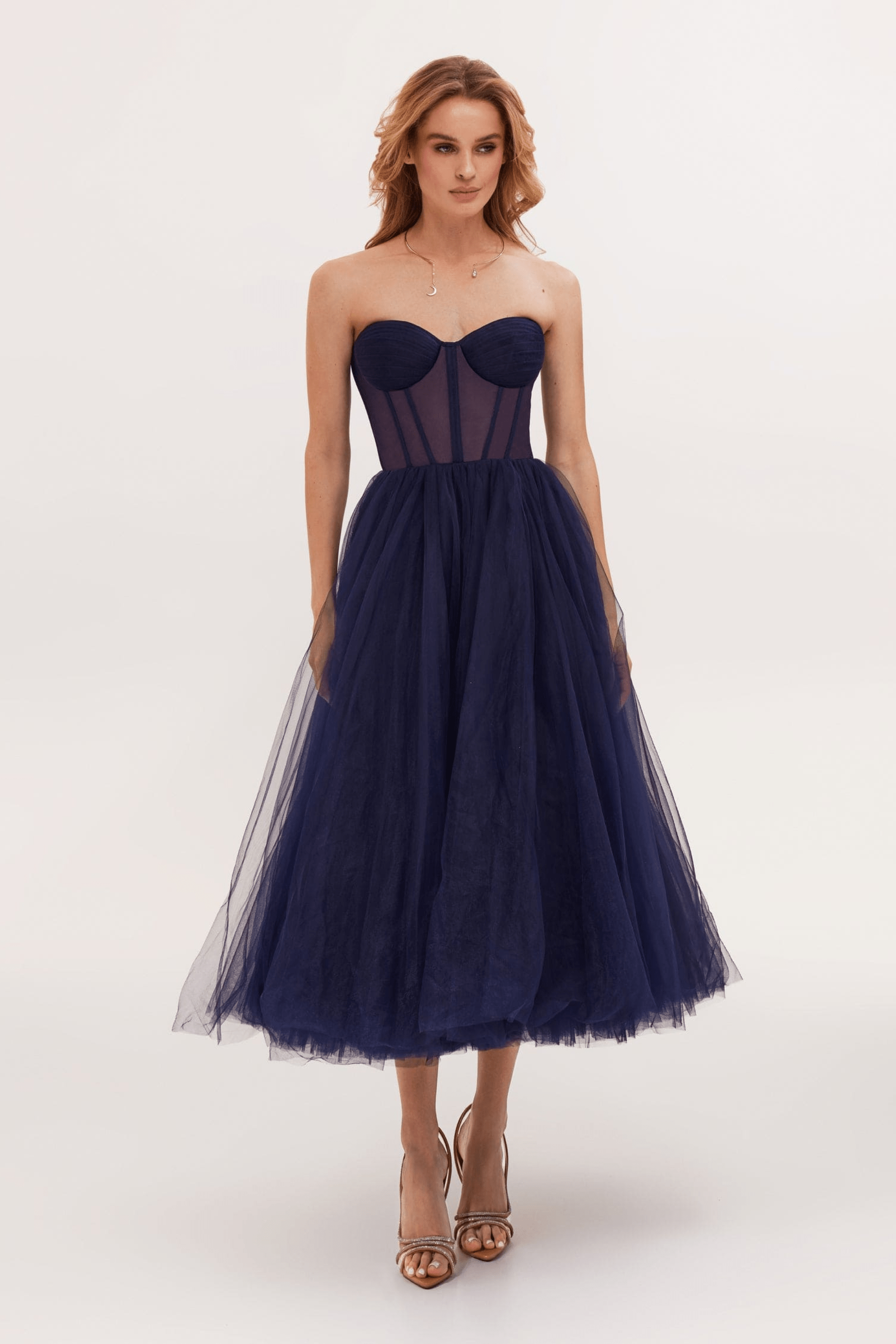 Robe bustier bleu marine en tulle, longueur mi-mollet, portée par une femme. Élégante et moderne, idéale pour soirées et événements formels.