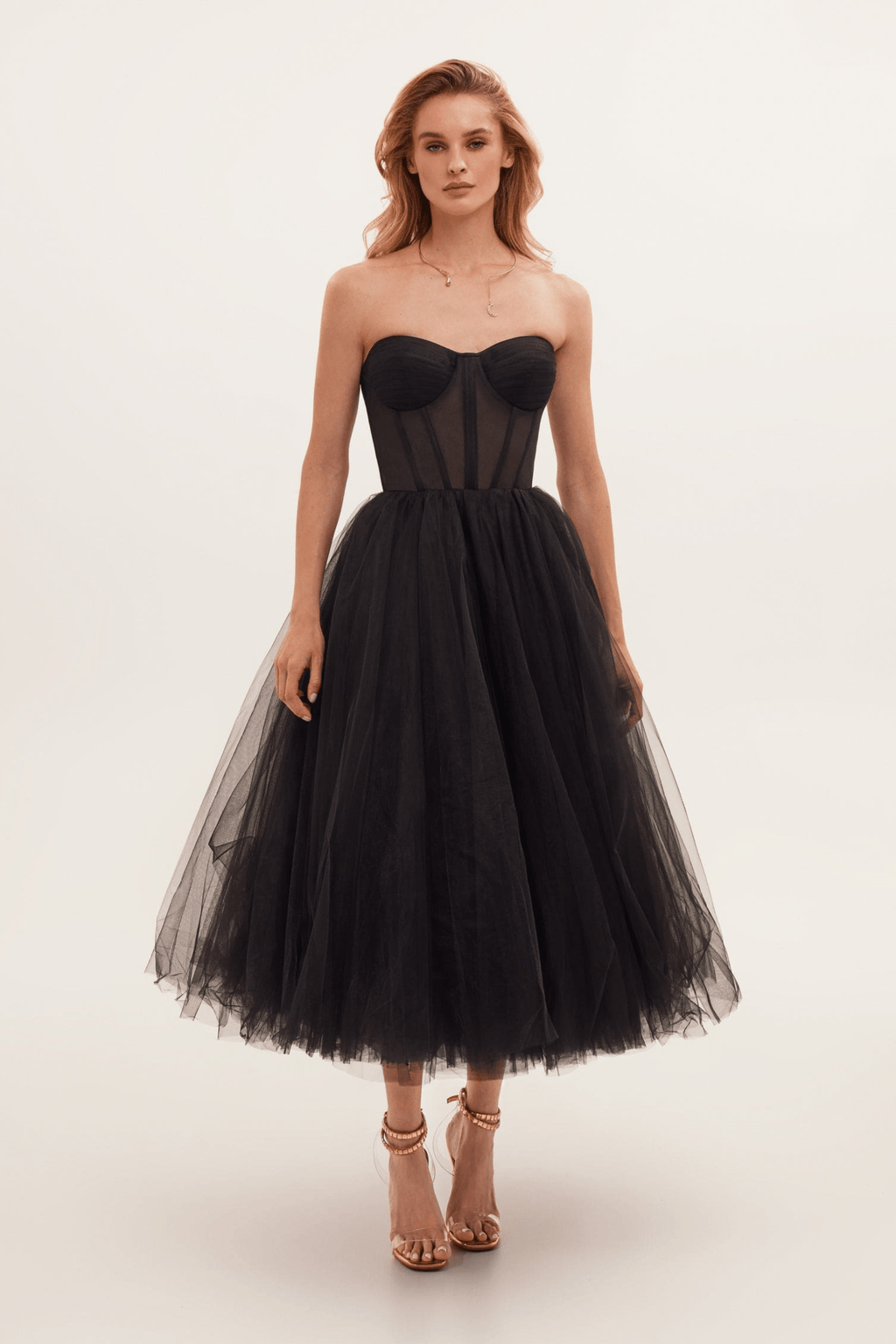 Robe bustier noire élégante en tulle, longueur mi-mollet, portée par une femme. Mode soirée chic, style glamour, tendance actuelle.