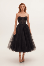 Robe bustier noire élégante en tulle, longueur mi-mollet, portée par une femme. Mode soirée chic, style glamour, tendance actuelle.