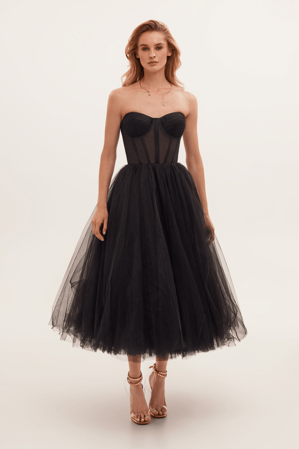 Robe bustier noire élégante en tulle, longueur mi-mollet, portée par une femme. Mode soirée chic, style glamour, tendance actuelle.