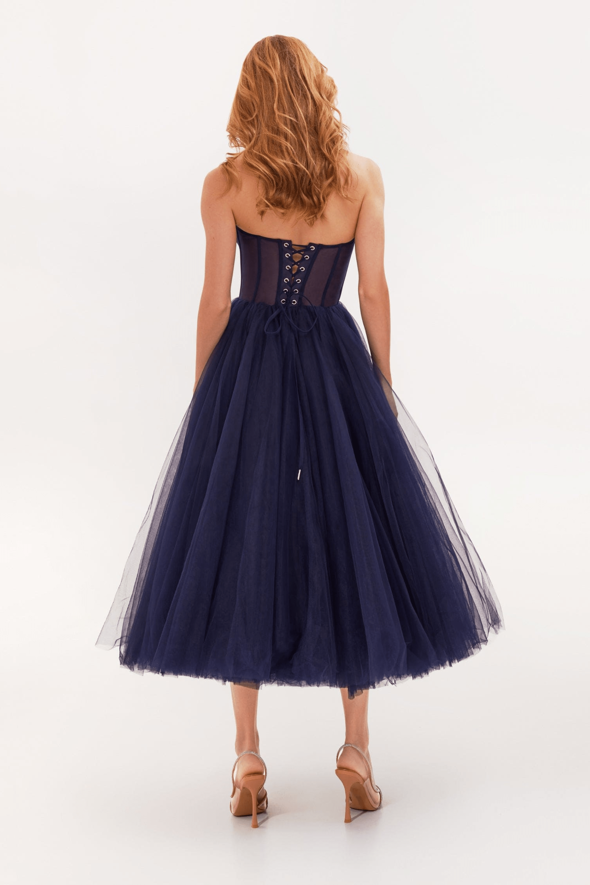 Robe bustier bleu marine en tulle, longueur mi-mollet, avec laçage au dos, portée par une femme aux cheveux roux, sur fond blanc.