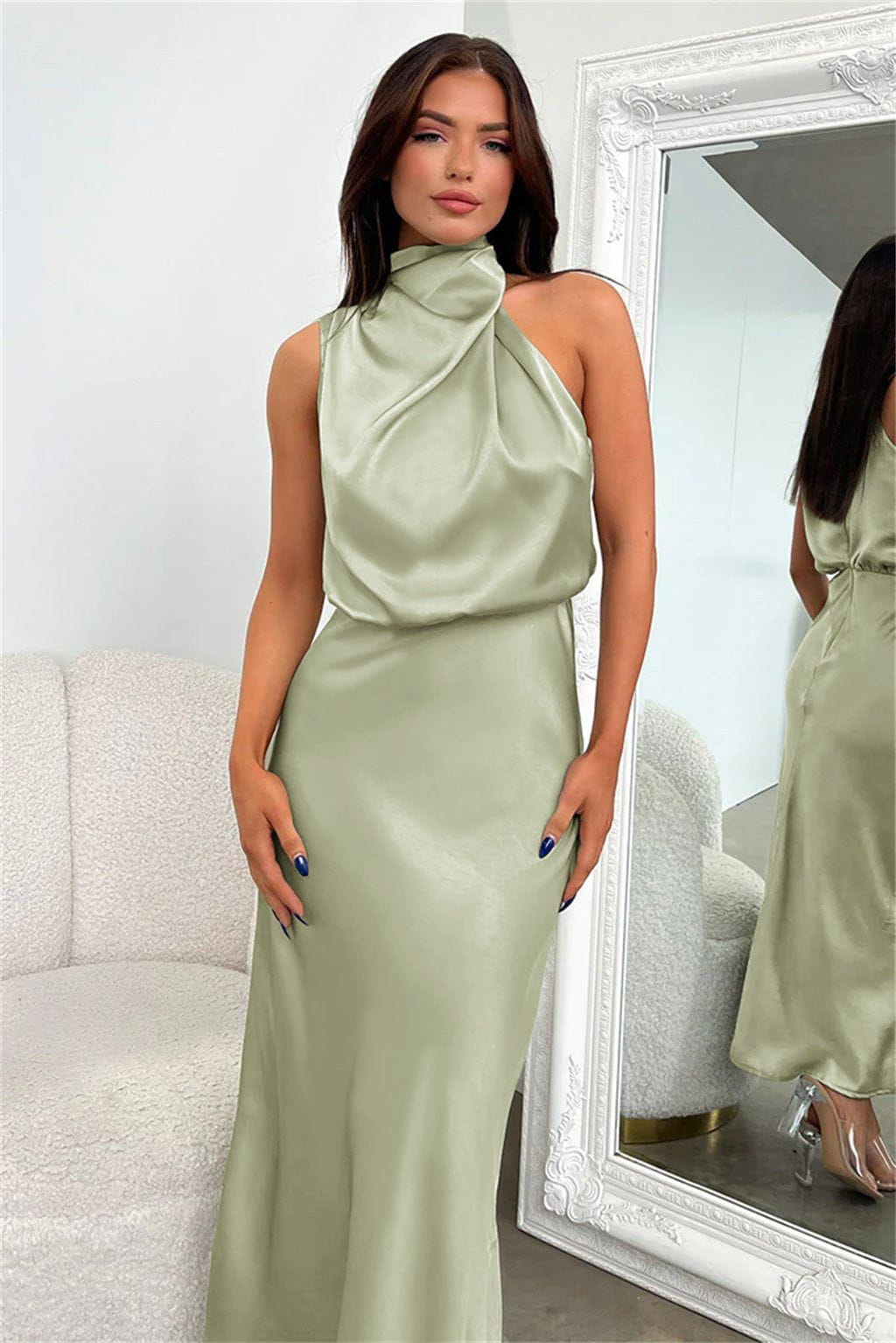 Robe longue satinée vert sauge, sans manches, col drapé, portée par une femme devant un miroir. Mode élégante, tendance soirée chic.
