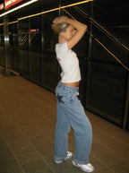 Jeune femme en jeans larges et t-shirt blanc posant dans une station de métro moderne, style urbain, mode décontractée, ambiance nocturne.