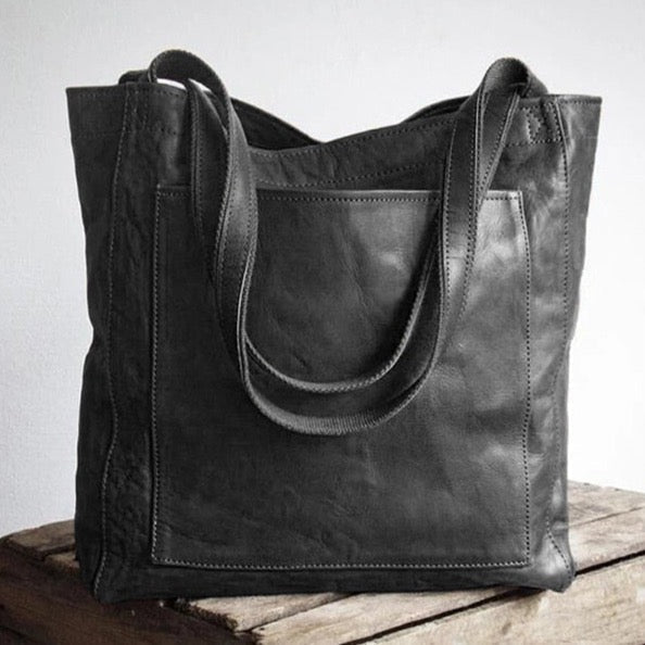 Sac cabas en cuir noir élégant sur fond neutre, avec anses robustes et design minimaliste. Accessoire mode tendance pour femmes.