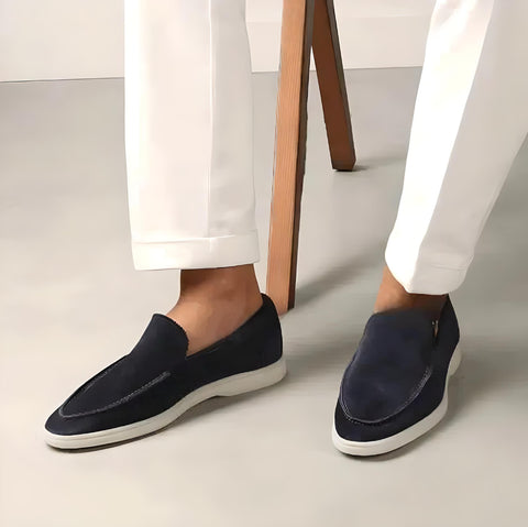 Chaussures mocassins en daim bleu marine pour homme, portées avec un pantalon blanc. Style élégant et moderne, parfait pour une tenue décontractée.