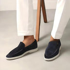 Chaussures mocassins en daim bleu marine pour homme, portées avec un pantalon blanc. Style élégant et moderne, parfait pour une tenue décontractée.