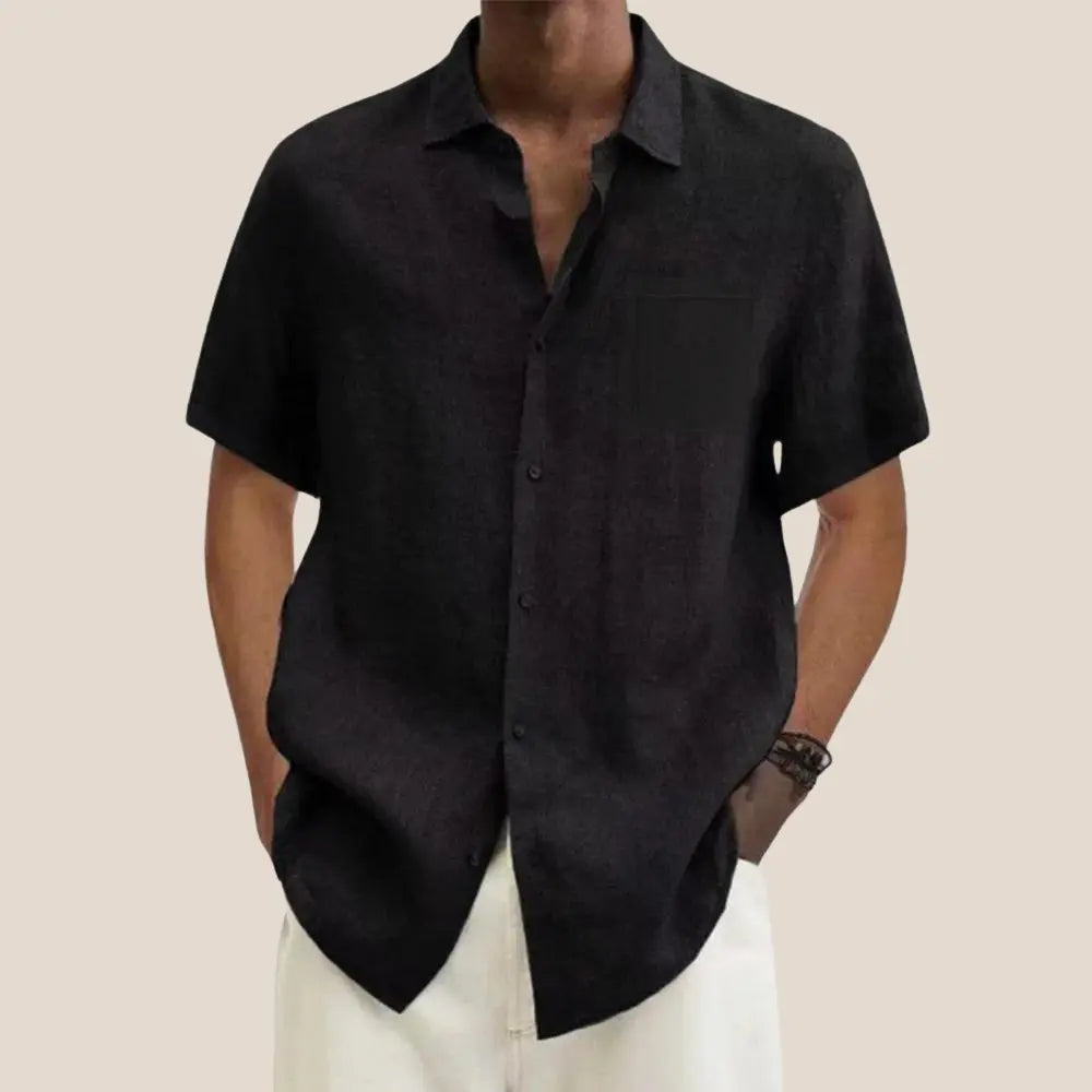 Chemise noire à manches courtes pour homme, style décontracté, col ouvert, tissu léger, portée avec un pantalon blanc, mode estivale élégante.