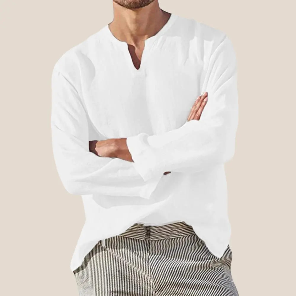 Homme portant une chemise blanche en lin à manches longues, col en V, bras croisés, sur fond beige. Mode masculine élégante et décontractée.