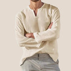 Homme portant une chemise en lin beige à col tunisien, manches longues, associée à un pantalon rayé gris. Mode masculine élégante et décontractée.