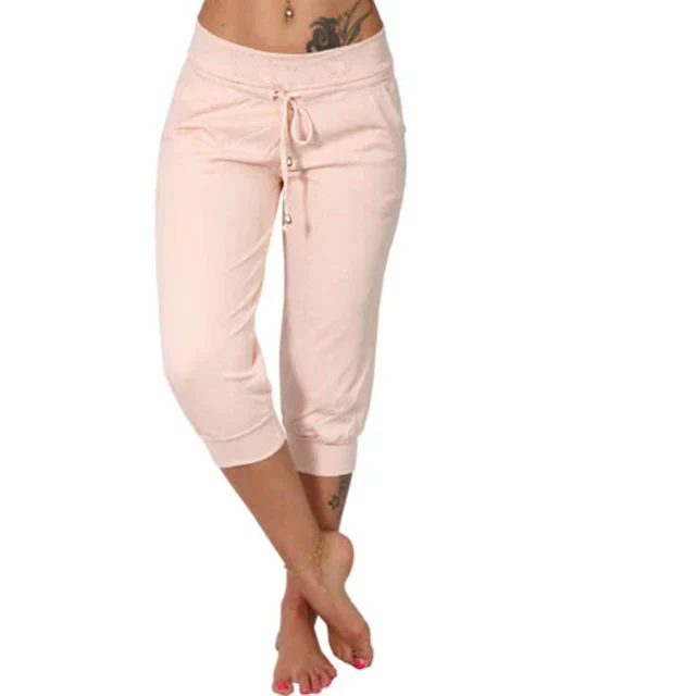 Femme portant un pantalon de jogging rose pâle, taille basse, avec cordon de serrage, pieds nus. Mode décontractée, tenue confortable.