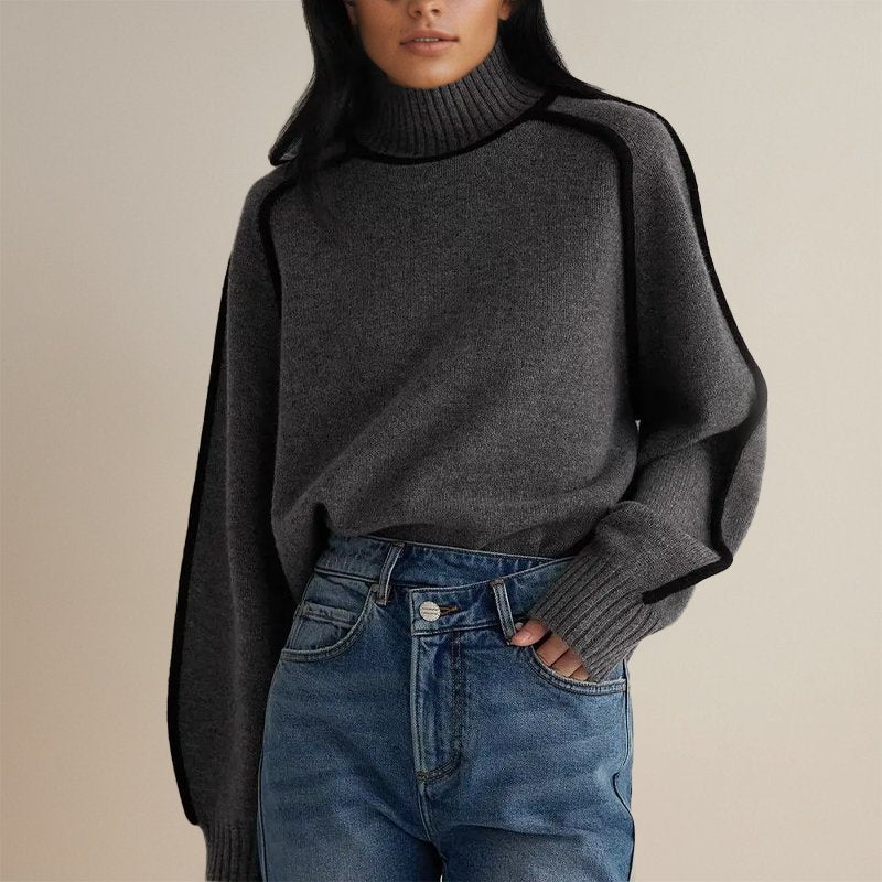 Femme portant un pull gris à col roulé et manches longues, associé à un jean bleu. Mode automne-hiver, style décontracté et élégant.