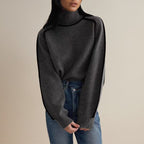 Femme portant un pull gris à col roulé et manches longues, associé à un jean bleu. Mode automne-hiver, style décontracté et élégant.