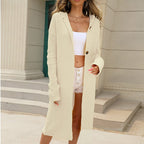 Femme portant un long cardigan beige à capuche, boutons en bois, sur un top blanc et un short. Mode automne, style décontracté chic.