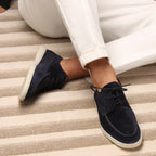 Chaussures bateau en daim bleu marine pour homme, portées avec un pantalon blanc, posées sur un tapis rayé beige. Mode masculine élégante.