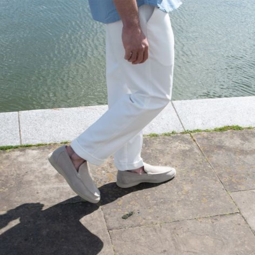 Homme marchant près de l'eau, portant un pantalon blanc et des chaussures beiges. Mode estivale, promenade au bord de l'eau, style décontracté.