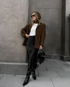Femme élégante en manteau marron, jupe noire et bottes, posant avec un sac à main noir. Mode urbaine chic, style automne-hiver tendance.