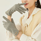 Femme portant des gants gris élégants, chemisier blanc à col plissé et gilet beige. Accessoire mode hiver, style chic et moderne.