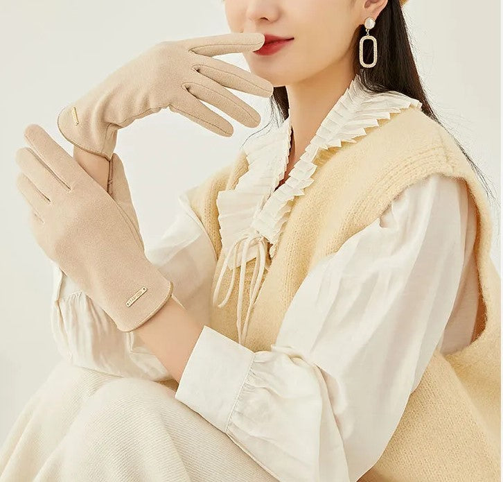 Femme élégante portant des gants beiges en laine, chemisier blanc à volants, pull sans manches beige, boucles d'oreilles pendantes, style automne chic.