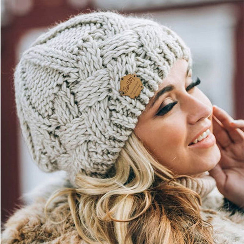 Femme souriante portant un bonnet en laine tricoté gris, style hiver, mode féminine, accessoire chaud, cheveux blonds bouclés, extérieur.