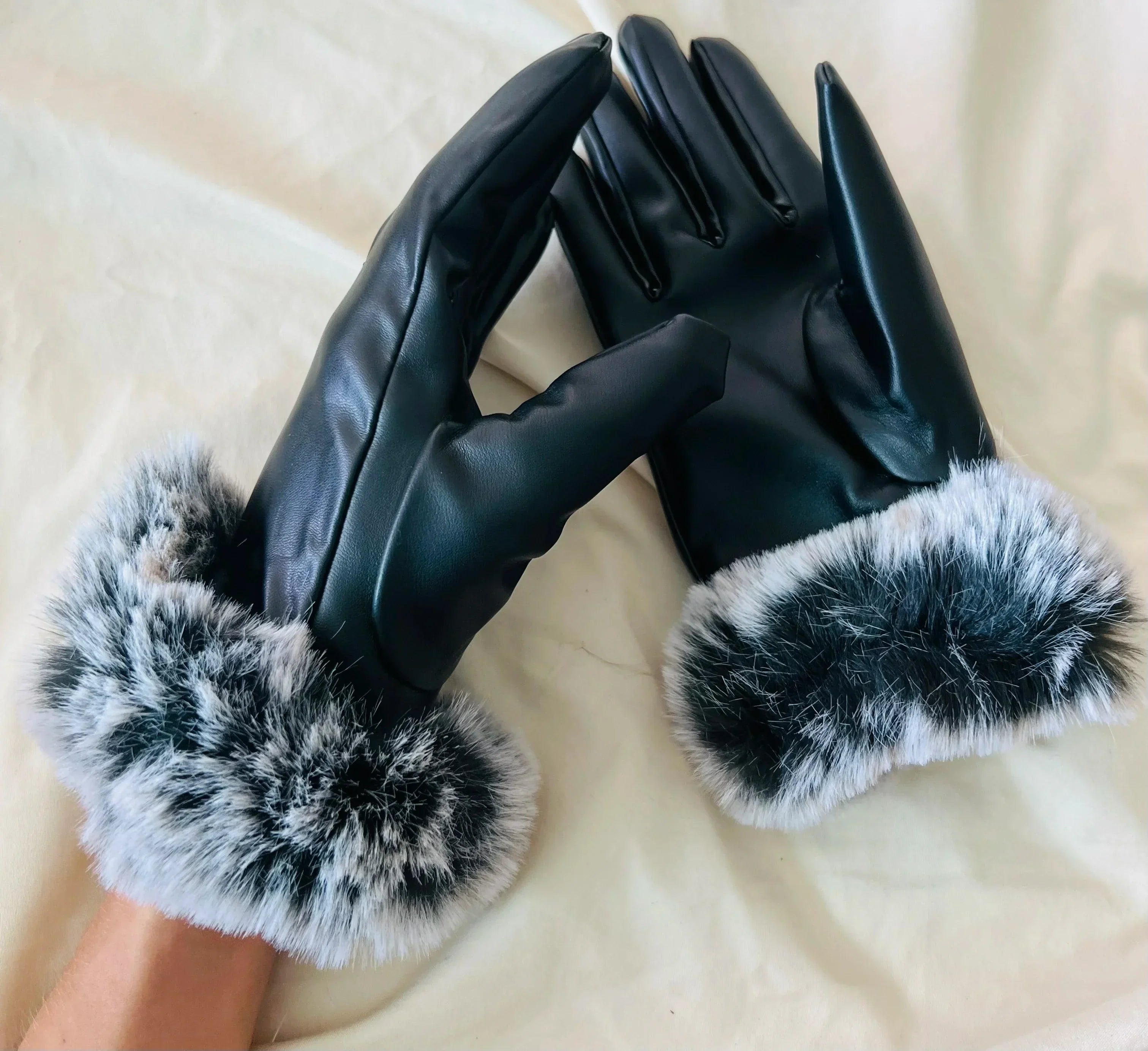 Gants en cuir noir avec doublure en fausse fourrure blanche et grise, posés sur un fond clair. Accessoire d'hiver élégant et chaud.