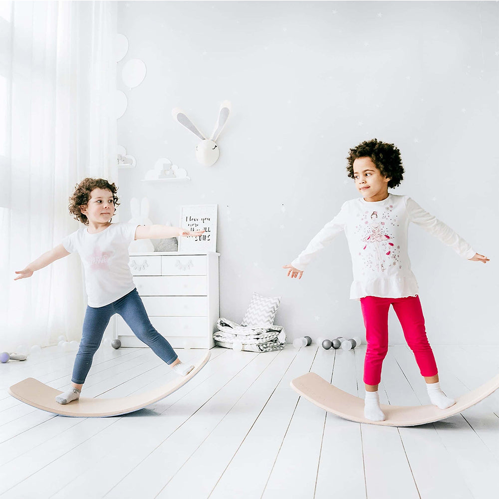Deux enfants jouent sur des planches d'équilibre en bois dans une chambre lumineuse, décorée de jouets et d'éléments scandinaves.