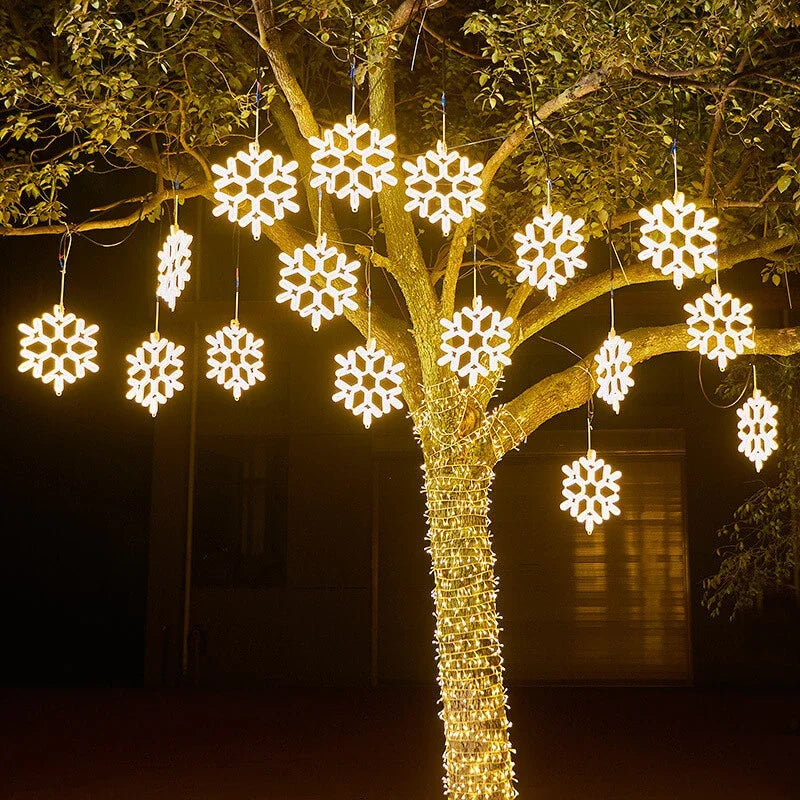 Arbre décoré de guirlandes lumineuses en forme de flocons de neige, illuminant la nuit. Décoration festive extérieure, éclairage LED.