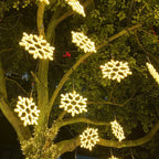 Guirlandes lumineuses flocon de neige LED accrochées à un arbre, éclairage extérieur décoratif, ambiance festive nocturne, jardin illuminé.