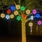 Arbre décoré de guirlandes lumineuses en forme de flocons multicolores, illuminant la nuit. Éclairage festif, décoration extérieure, ambiance Noël.