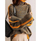Femme portant un pull en maille épaisse à col roulé, rayures orange, avec un sac à main noir matelassé. Mode automne-hiver tendance.