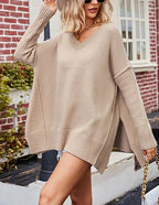 Femme portant un pull oversize beige, manches longues, devant une maison en briques rouges. Mode automne, style décontracté, tendance féminine.