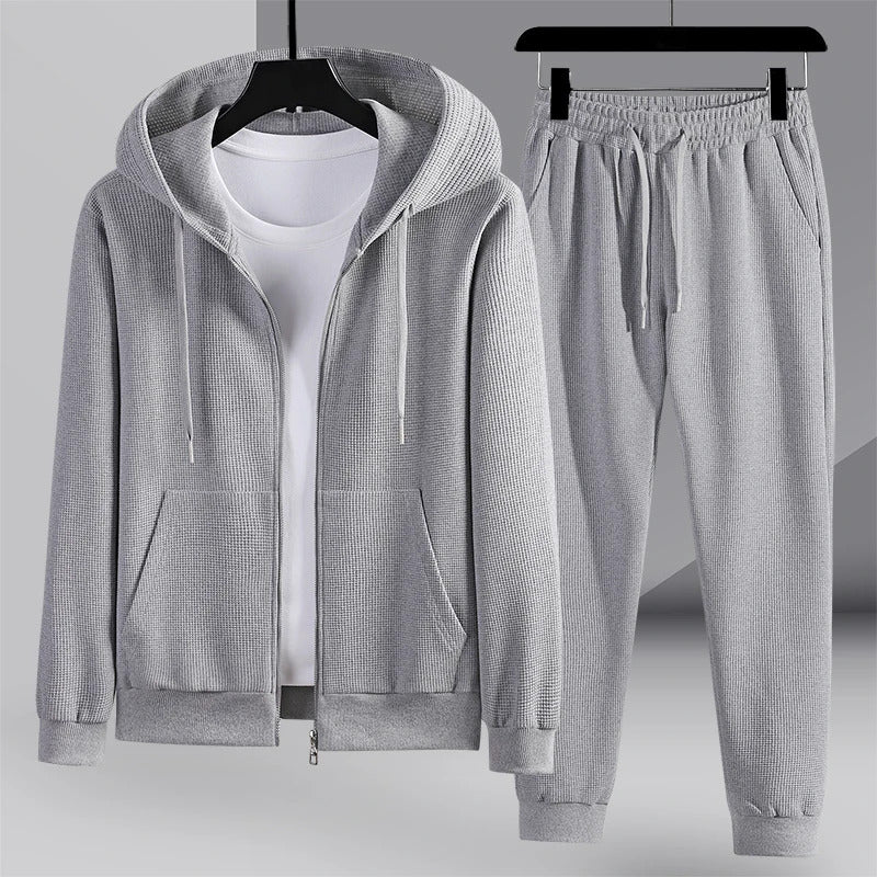 Survêtement gris pour homme avec capuche, fermeture éclair et poches, accompagné d'un pantalon assorti. Ensemble confortable et moderne.