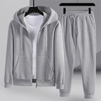 Survêtement gris pour homme avec capuche, fermeture éclair et poches, accompagné d'un pantalon assorti. Ensemble confortable et moderne.
