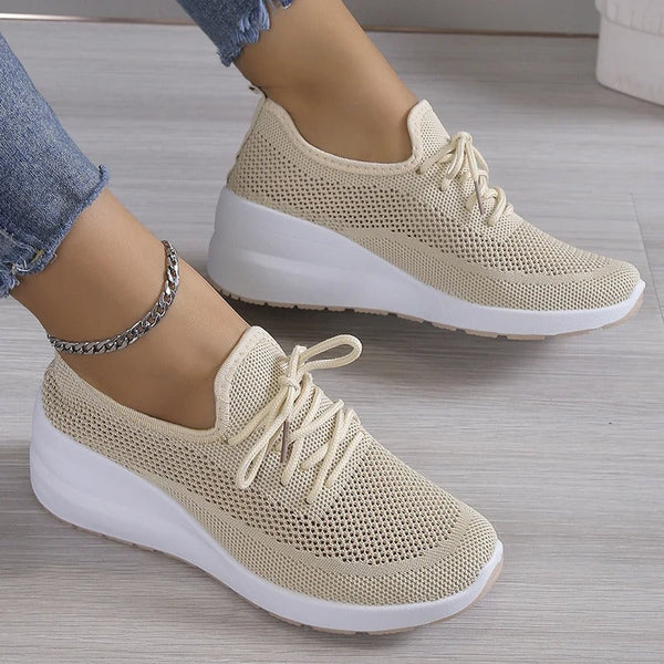 Chaussures de sport beiges en maille respirante avec semelle blanche, portées avec un jean et un bracelet chaîne argenté à la cheville.