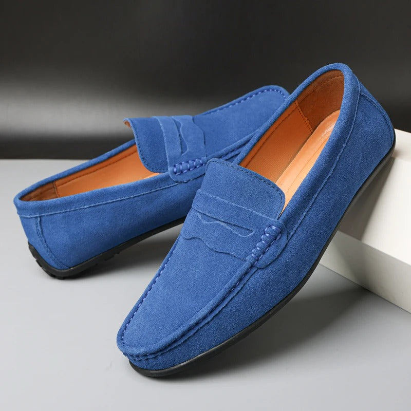 Mocassins en daim bleu pour homme, élégants et confortables, posés sur une surface grise. Chaussures tendance, idéales pour un look décontracté.