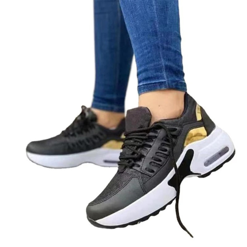 Chaussures de sport noires et blanches avec détails dorés, portées avec un jean bleu. Sneakers modernes, tendance, confortables pour la marche.