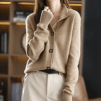 Femme portant un cardigan en laine beige avec boutons, manches longues, col rabattu, posant dans un intérieur moderne. Mode automne-hiver élégante.