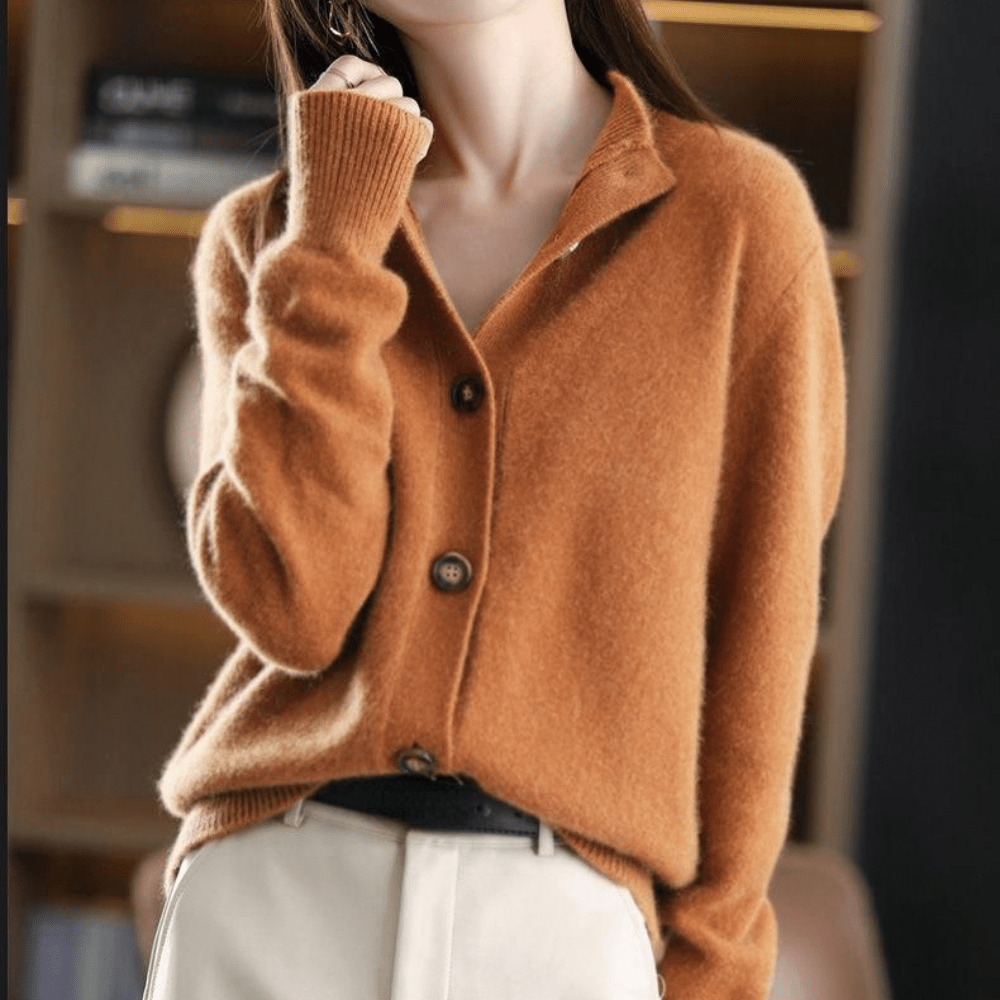 Femme portant un cardigan en laine marron, manches longues, col ouvert, boutons en bois, style automne-hiver, devant une étagère floue.