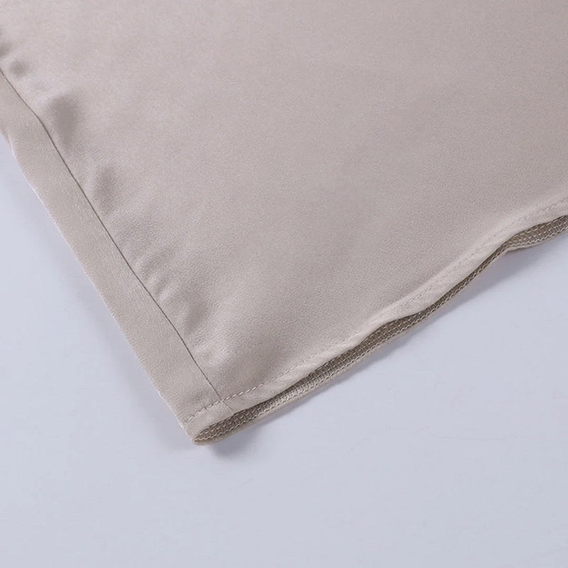 Coin d'une taie d'oreiller en satin beige, texture lisse et brillante, idéale pour soins capillaires et peau, luxe et confort pour chambre à coucher.