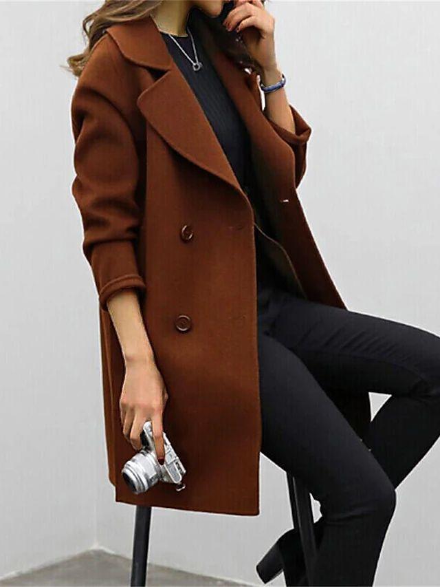 Femme portant un manteau marron élégant, assise avec un appareil photo argenté à la main, tenue chic et moderne, mode automne-hiver.