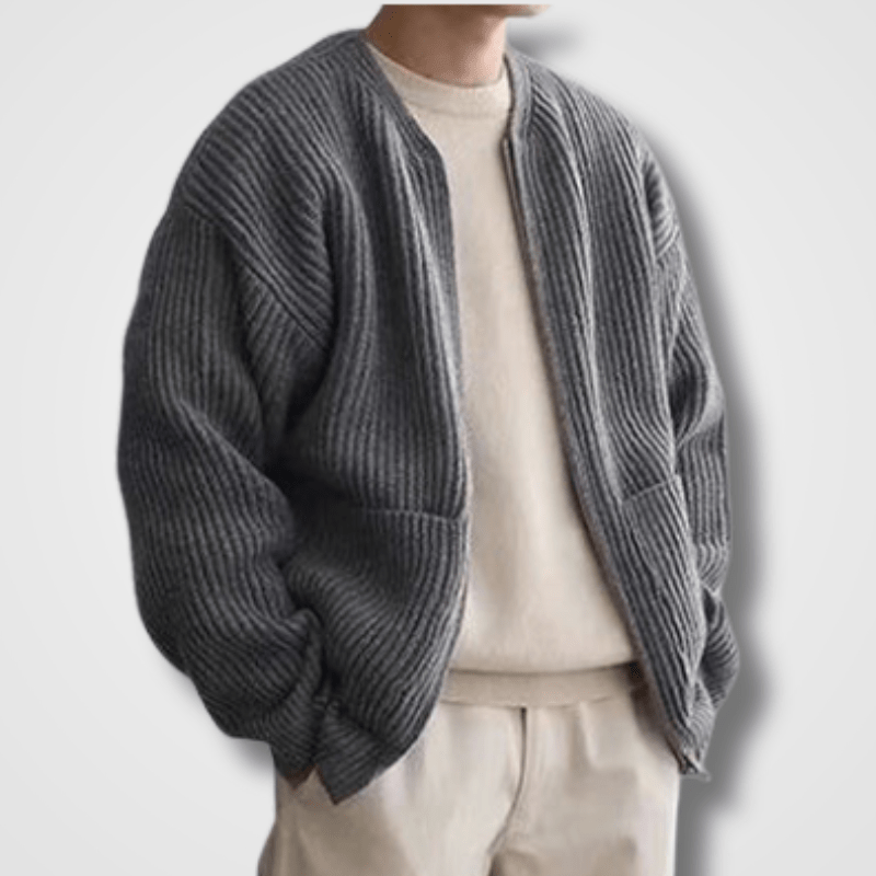 Homme portant un cardigan gris en maille épaisse, style décontracté, sur un pull beige et un pantalon assorti. Mode automne-hiver tendance.