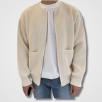 Homme portant un cardigan beige en maille avec poches, sur un t-shirt blanc et un jean bleu. Mode masculine décontractée, style automne-hiver.