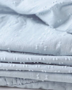 Tissu en coton bleu clair texturé avec motifs à pois, idéal pour couture et décoration intérieure. Matériau doux et élégant pour vêtements.