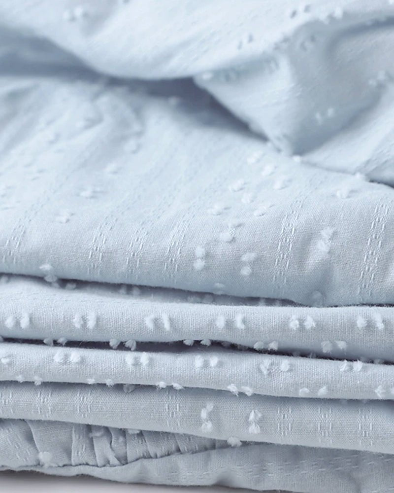 Tissu en coton bleu clair texturé avec motifs à pois, idéal pour couture et décoration intérieure. Matériau doux et élégant pour vêtements.