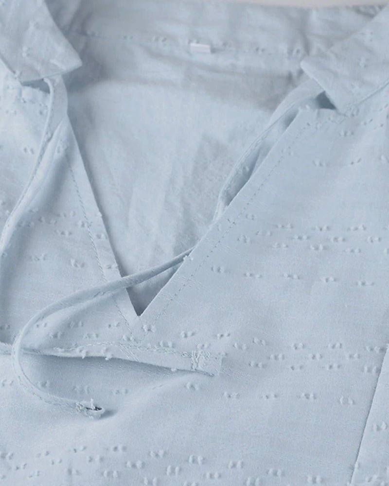 Chemisier bleu clair en coton avec col en V et lacets, motif broderie anglaise. Mode féminine, style décontracté, tendance printemps-été.