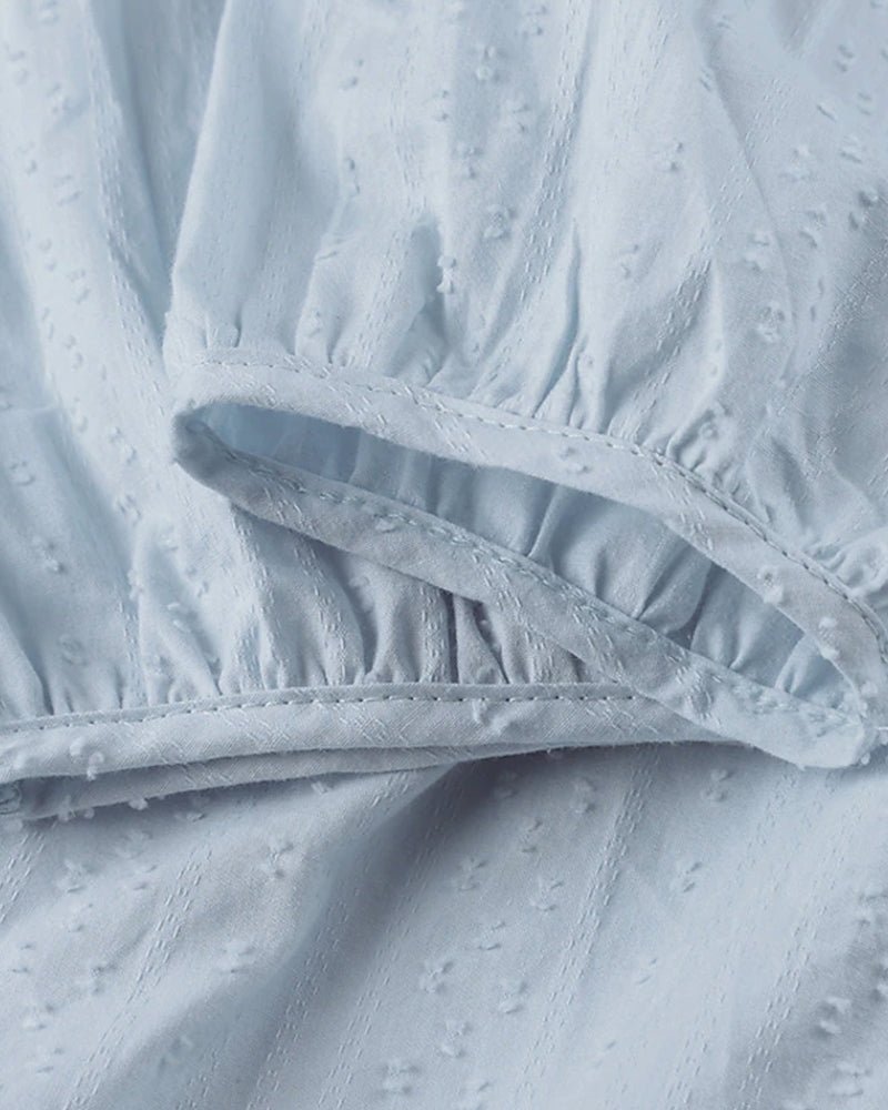 Robe en coton bleu clair avec texture à pois, manches bouffantes et détails plissés. Mode féminine élégante, tissu léger et confortable.